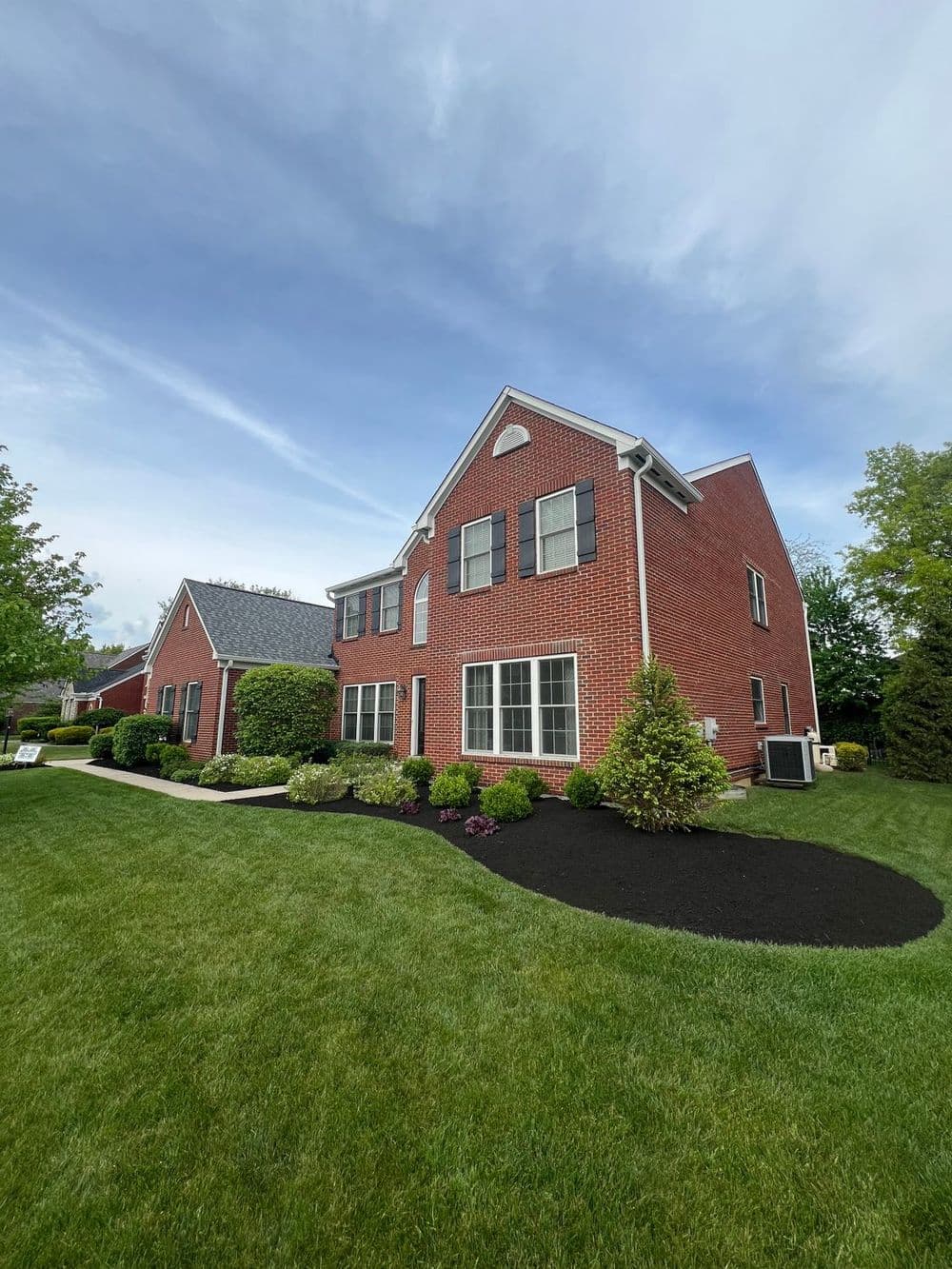 Brick house with manicured lawn and landscaping, against a blue sky. Ideal suburban home.