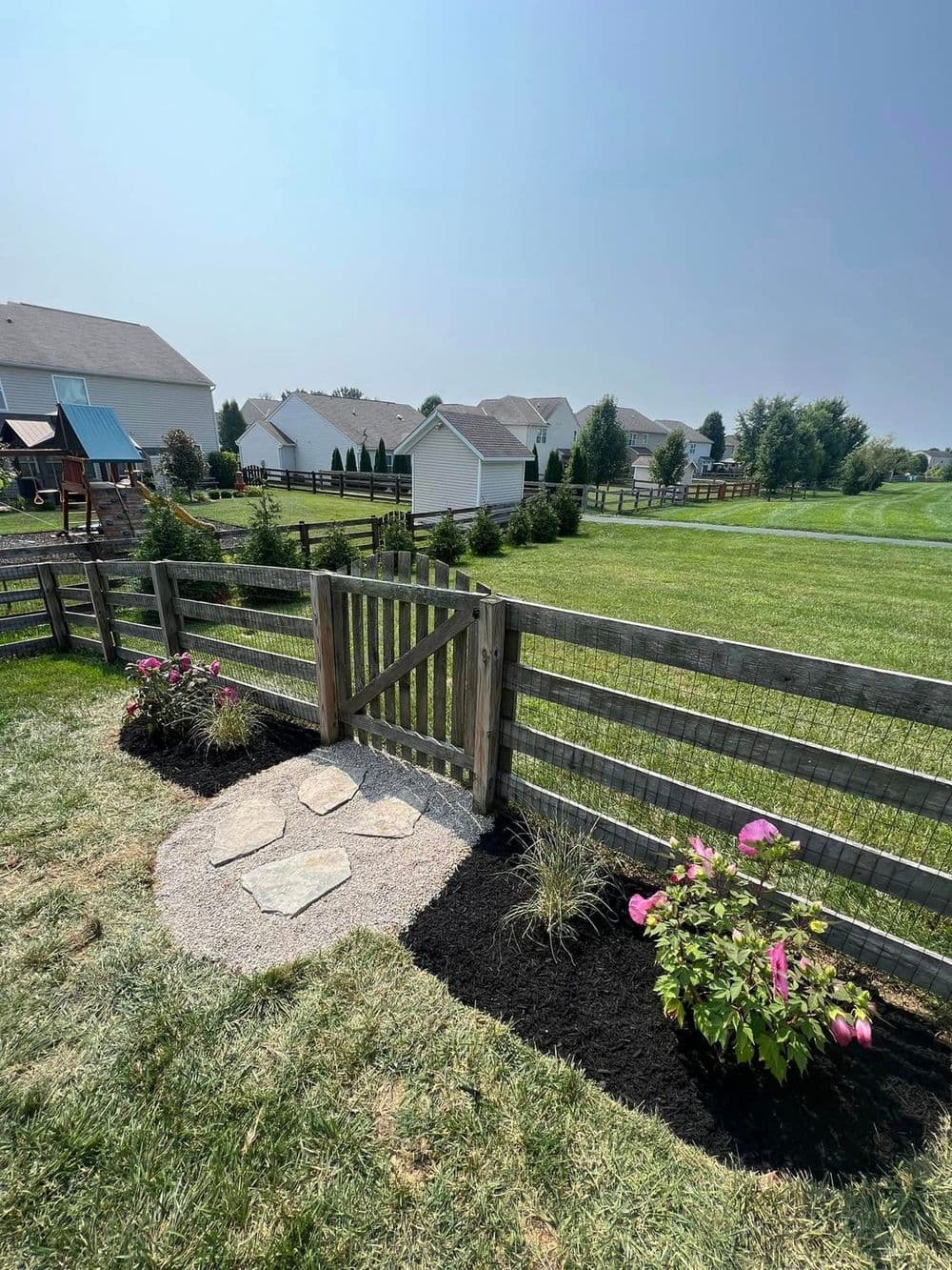 Wooden fence gate leading to a well-maintained yard with stone pathway and colorful flowers.
