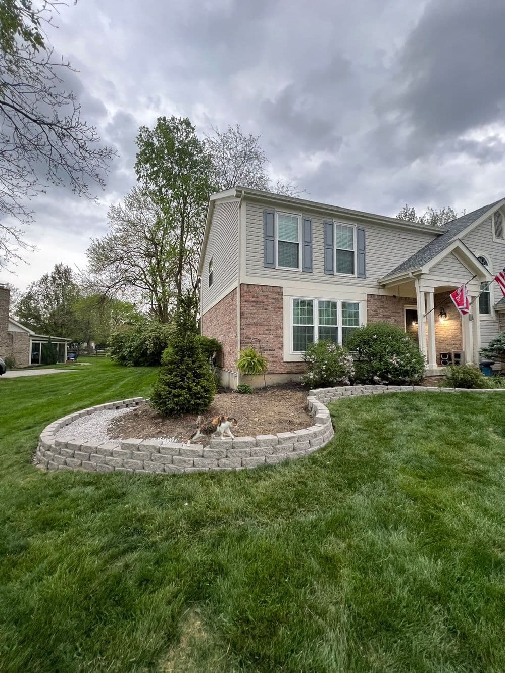 House with brick exterior and landscaping, featuring a dog in a garden under cloudy skies.