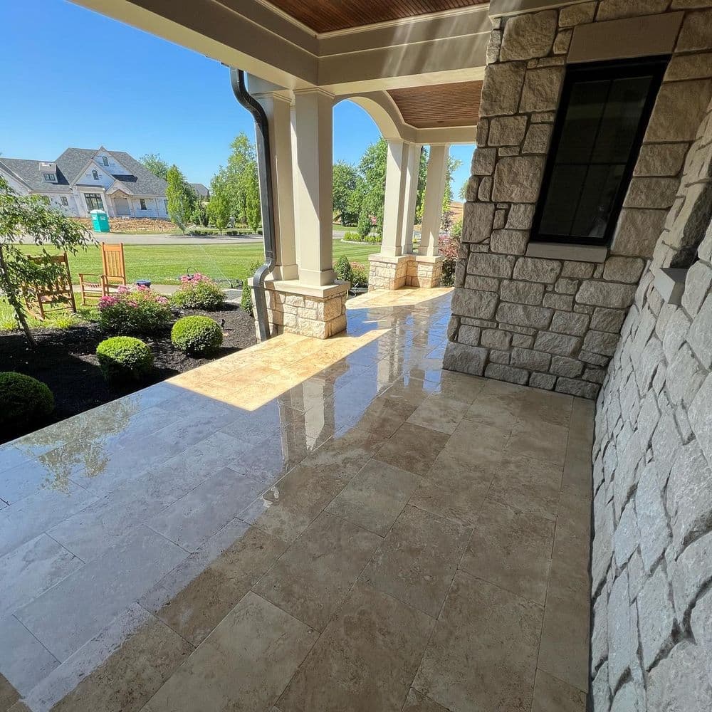 Polished stone entrance porch with landscaping, featuring sunlight and a welcoming residential view.