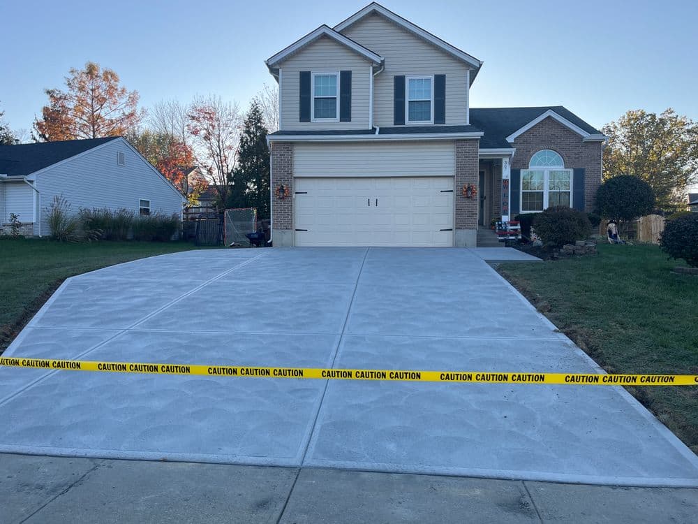 Newly poured driveway with caution tape in front of a suburban house.