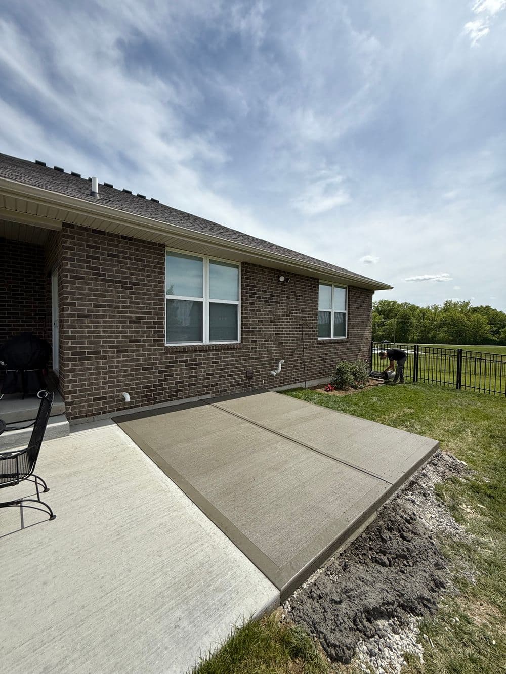 Newly poured concrete patio next to a brick house, with a grassy yard and blue sky.