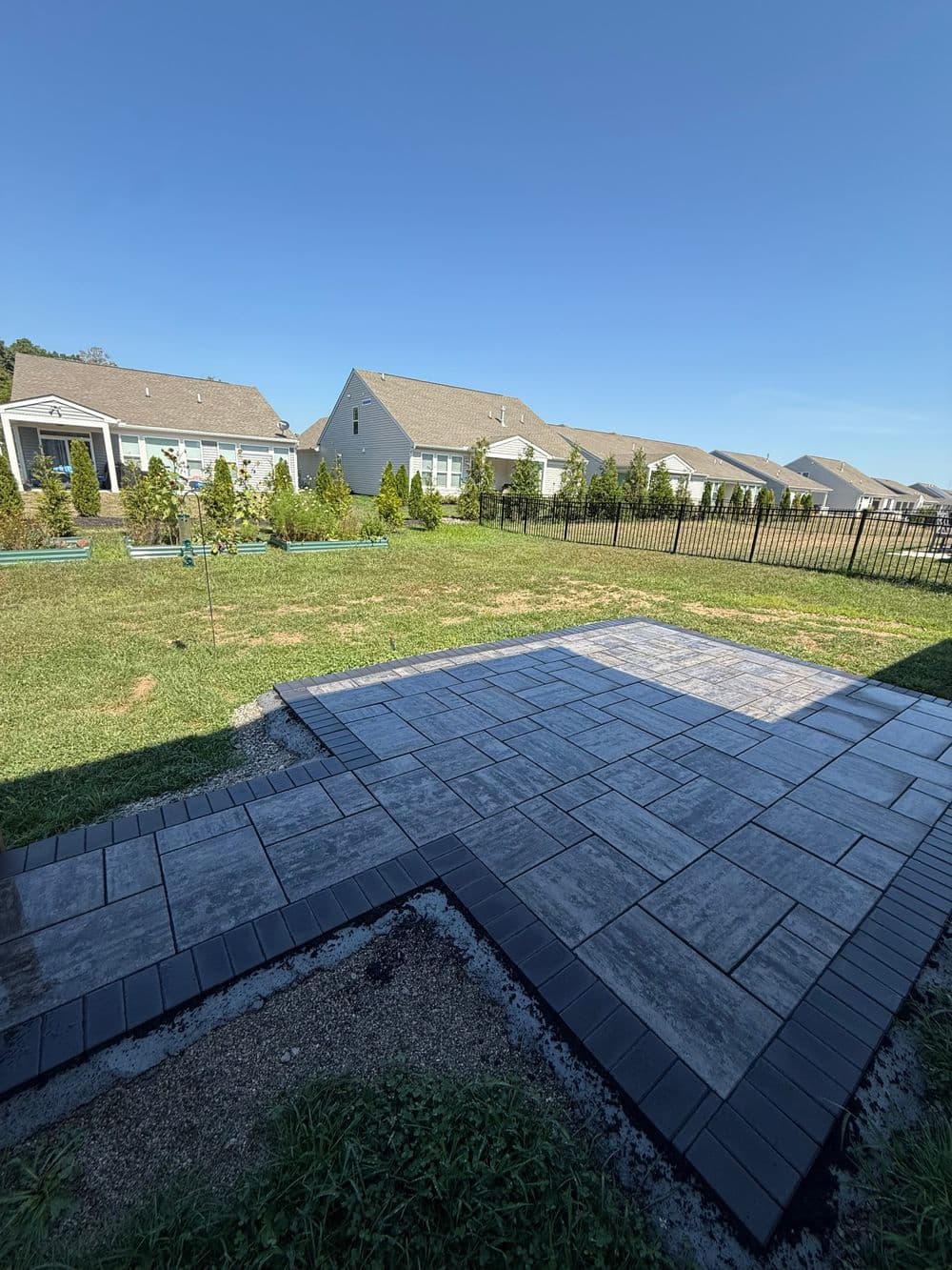 Newly installed paver patio in a backyard with green grass and residential houses in the background.
