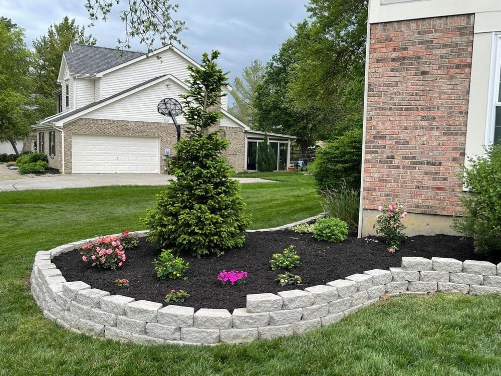Landscaped garden with shrubs, flowers, and a brick border next to a house.