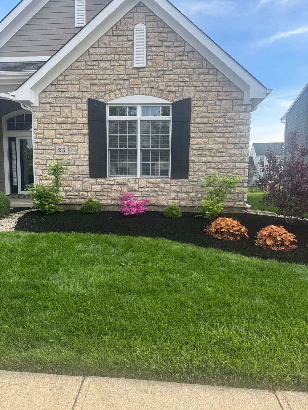 Front view of a landscaped home with stone exterior, colorful flowers, and green lawn.