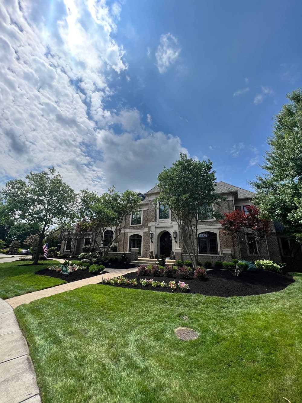 Elegant brick home with lush landscaping and a vibrant garden under a sunny sky.