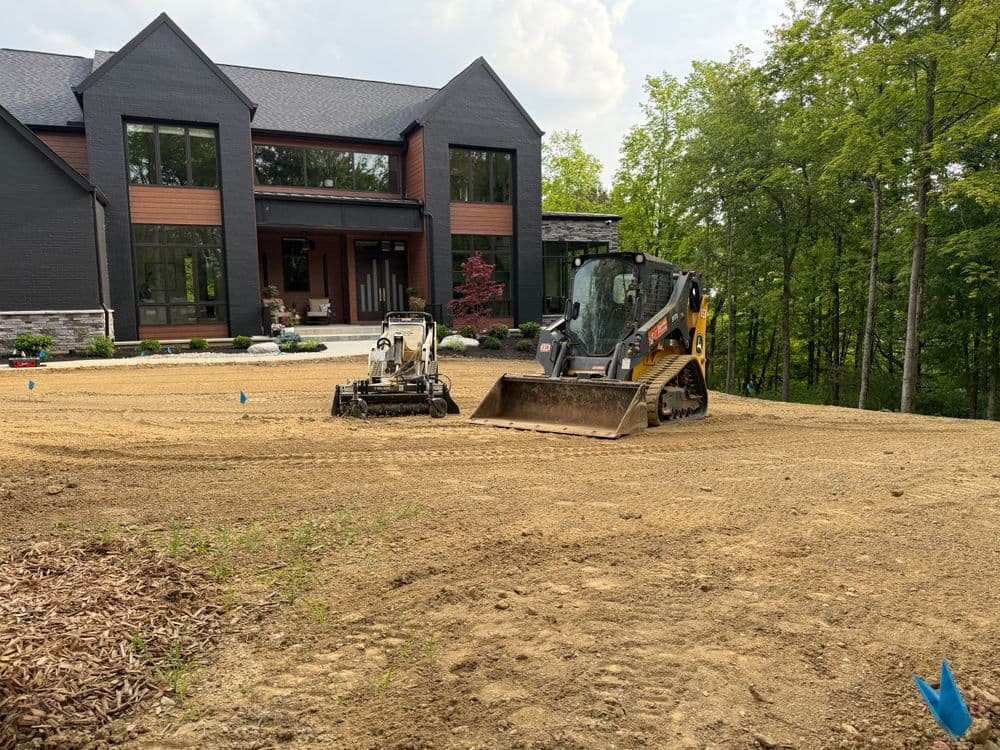 Construction site with a skid steer and mini excavator preparing landscape near a modern home.