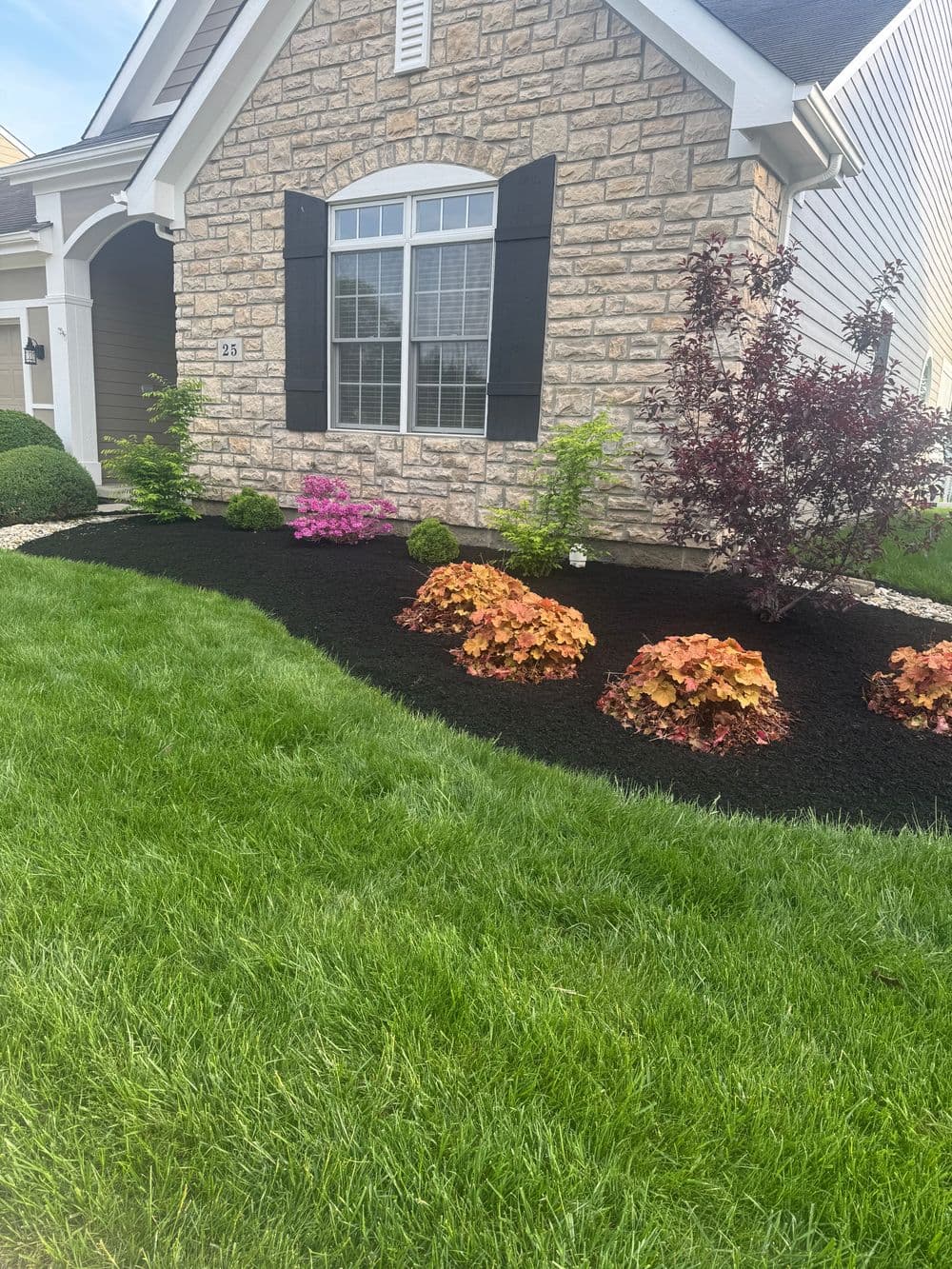Colorful landscaping with stone house, green grass, and vibrant flower beds.