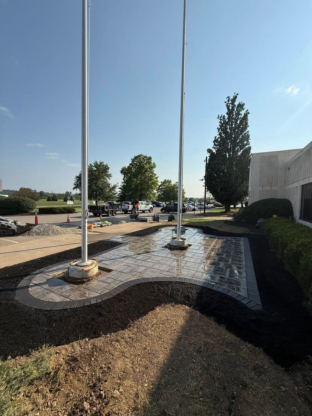 Newly landscaped area with flagpoles, featuring patterned paving and freshly laid mulch.