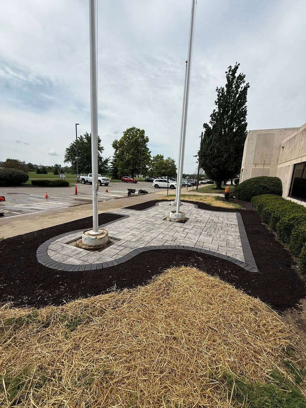 Landscaped area with paver stone design and flagpoles in a parking lot.