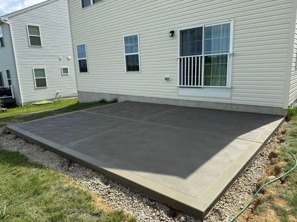 Newly poured concrete patio with textured surface behind a residential building.